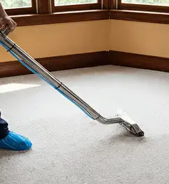 Steam carpet cleaning technician using a hot-water extraction wand on a residential carpet, wearing blue protective shoe covers Pembroke Pines, FL.