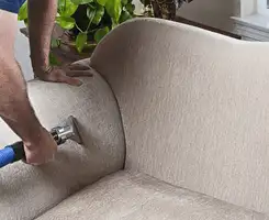 Professional upholstery cleaner deep-cleaning a fabric sofa with a handheld extraction tool and hose in Pembroke Pines, FL.